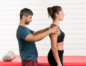 Male osteopath doing a postural evaluation on a young female patient assessing the alignment of her vertebrae and spine in an alternative medicine and healthcare concept